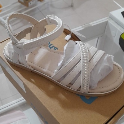 Sandália branca infantil com tiras e pérolas sobre caixa de cartão