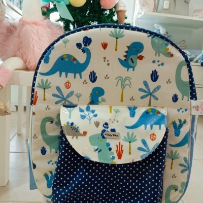 mochila infantil com padrão de dinossauros e bolso azul com bolinhas brancas