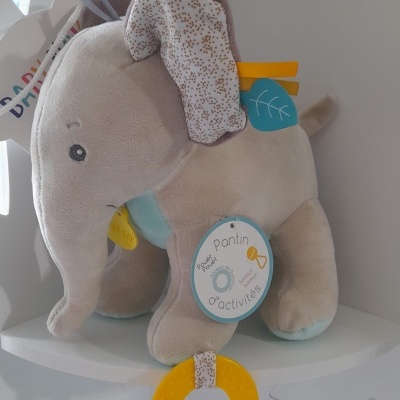 Elefante de peluche cinzento com detalhes coloridos e argola amarela pendurada