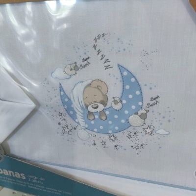Lençol branco para berço com bordado de urso a dormir numa lua azul com bolinhas brancas e ovelhas pequenas.