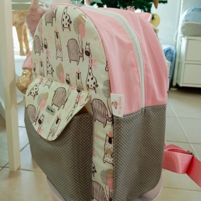 Mochila infantil rosa e cinza com padrão de animais e bolinhas branca colocada numa sala com decoração de Natal.