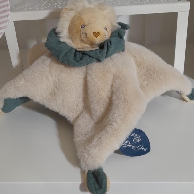 Pelúcia de leão bege com detalhes verdes e etiqueta azul