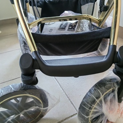 Carrinho de bebé com estrutura dourada, tecido preto e rodas protegidas por plástico