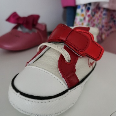 Sapato infantil branco e vermelho em destaque com sapato rosa ao fundo