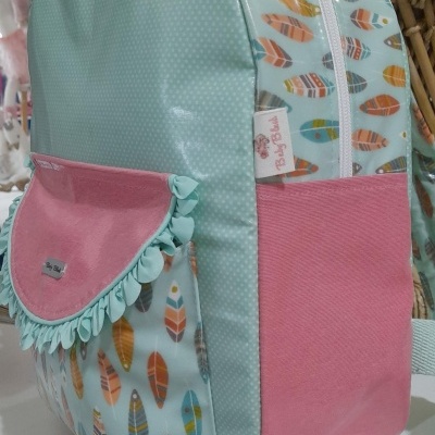 Mochila colorida com padrão de penas e bolso frontal rosa com franjas azuis