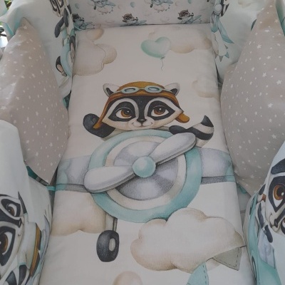 Berço branco com proteção acolchoada estampada com guaxinim em avião e nuvens