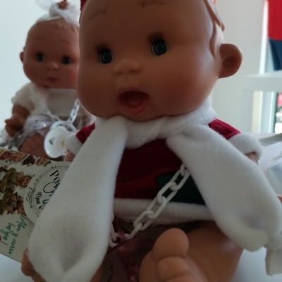 Boneca de plástico vestida com roupa vermelha e branca, chupeta presa com corrente branca