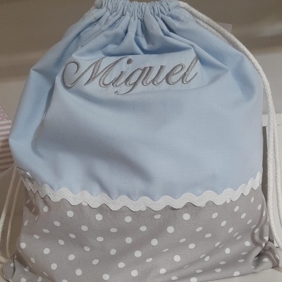 Mochila azul claro e cinza com padrão de bolinhas e nome Miguel bordado