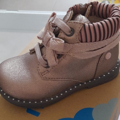 Bota infantil rosa com atacadores e sola preta sobre caixa de cartão