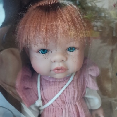 Boneca ruiva com olhos azuis vestida de rosa vista através de vidro