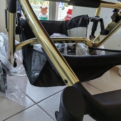 Estrutura dourada de carrinho de bebé com tecido e rodas pretas