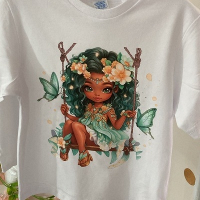 T-shirt branca com ilustração colorida de menina num baloiço com flores e borboletas