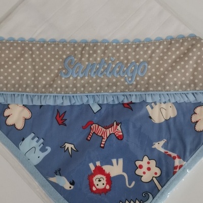 Fralda branca com faixa bege de bolinhas, nome Santiago bordado em azul e tecido azul com animais desenhados