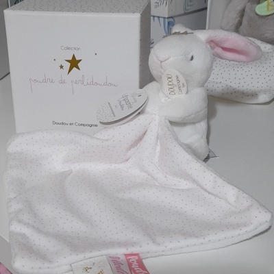 Objeto de tecido branco com padrão de pontos cor-de-rosa e cabeça de coelho com orelhas rosa, caixa branca ao lado.