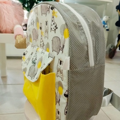 Mochila infantil com padrão de animais e bolso amarelo em ambiente interno
