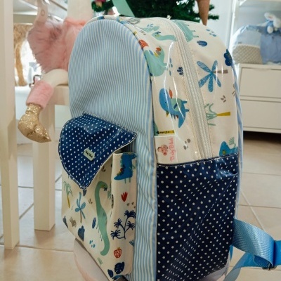 mochila infantil com padrão de dinossauros e bolso azul com bolinhas branca e cadeira rosa