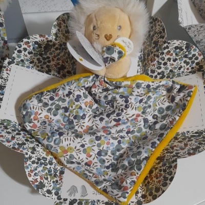 Mantas para bebé com estampado floral colorido e bordas amarelas, uma com brinquedo de pelúcia leão em caixa branca decorada