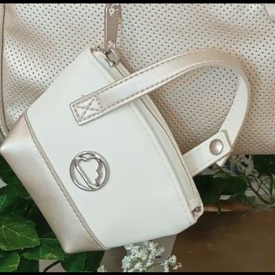 Bolsa pequena creme com detalhes bege e emblema metálico pendurada