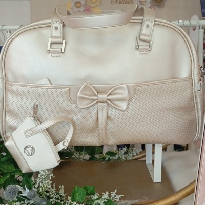 Bolsa creme elegante com laço e pequeno acessório pendurado, decorada com flores e plantas, texto 'Baby Blush' ao fundo