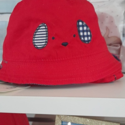 Chapéu vermelho infantil com detalhes bordados azuis e brancos numa prateleira