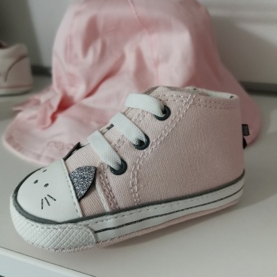 Ténis de bebé rosa claro com rosto de animal e chapéu rosa ao fundo