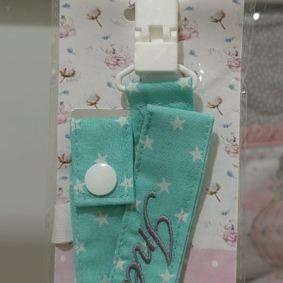 Tira azul turquesa com estrelas brancas e clipe de plástico branca em embalagem rosa com pontos e floral