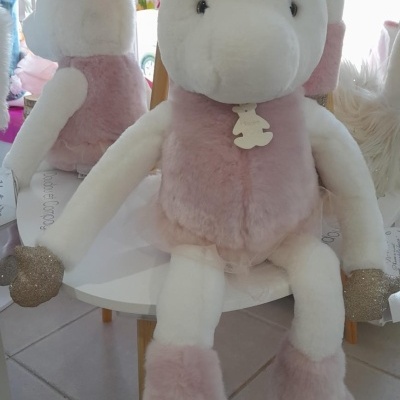 Boneco de peluche unicórnio branco com roupa rosa e detalhes dourados sentado numa cadeira