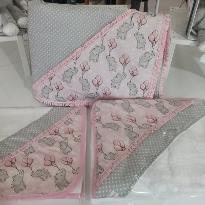 Toalhas de bebé cinza, branco e rosa com coelhinhos e bolinhas expostas numa mesa branca