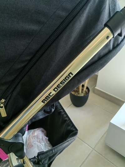 Carrinho de bebé com estrutura metálica dourada e tecido preto, texto ABC DESIGN visível