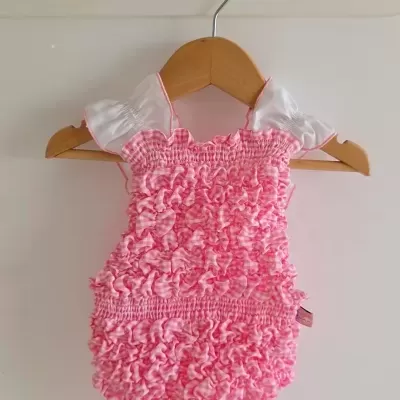 Fato de banho de bebé rosa xadrez com alças brancas pendurado num cabide de madeira