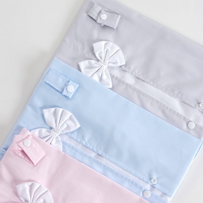 Peças de roupa para bebé em cinzento, azul e rosa com laços brancos.