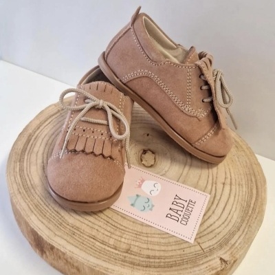 Sapatinhos de bebé em camurça castanha com atacadores e franjas sobre suporte de madeira redondo