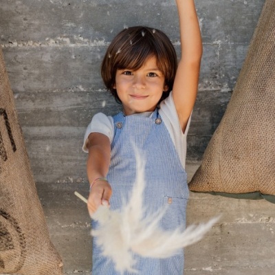Criança com macacão de riscas azuis e brancas segurando pena branca
