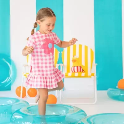 menina com vestido rosa de padrão xadrez e flor, a brincar em insuflável azul num ambiente colorido