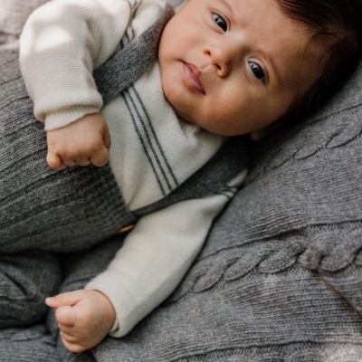 Bebé vestido com camisola branca e suéter cinza de malha deitada sobre manta cinza