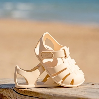 Sandálias de criança bege claro em plástico, com fecho velcro 'igor', sobre tronco na praia.