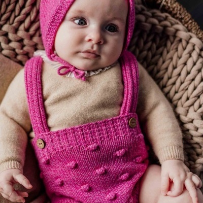 Bebé com roupa de malha rosa e bege sentado em cadeira de rattan
