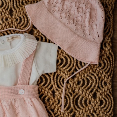 Conjunto de roupa de bebé rosa e branco sobre tapete de corda