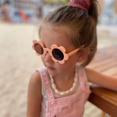 Criança com óculos de sol rosa florais e macacão rosa claro em ambiente externo