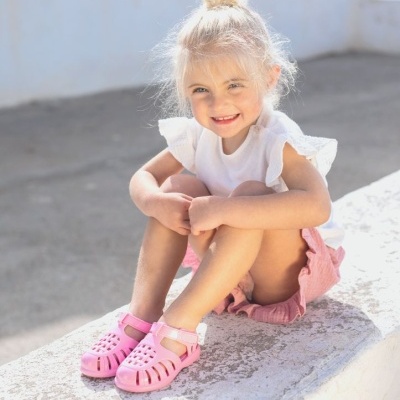 Menina pequena sentada com t-shirt branca, calções rosas e sandálias rosas