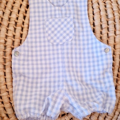 Macacão de bebé azul xadrez com botões em fundo de palha trançada