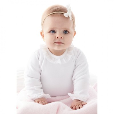 Bebé com body branco e faixa de cabelo sai laço sentada com manta rosa