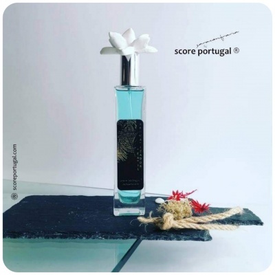 Frasco de perfume azul com tampa decorada, sobre pedra preta com elementos naturais