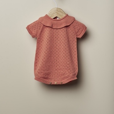 Body de bebé cor de rosa velho em malha com padrão perfurado e gola arredondada pendurado em cabide de madeira