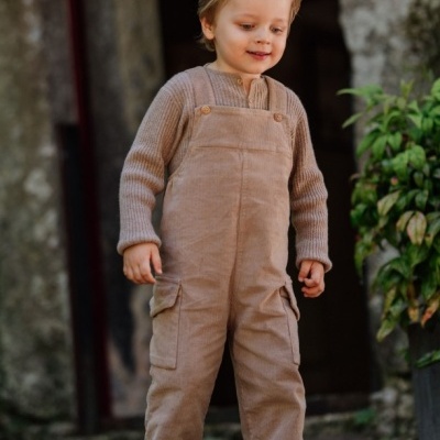 Criança com macacão de veludo cotelê castanho claro e camisa de malha castanha clara ao ar livre