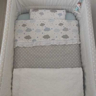 Berço branco com roupa de cama cinza e branca com padrões de estrelas e nuvens