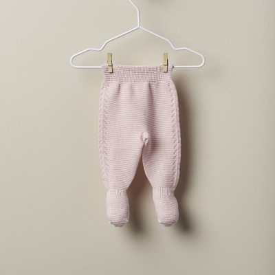 Calças de bebé rosa claro em malha penduradas num cabide branco