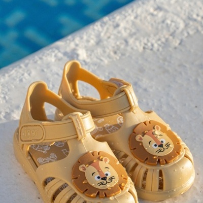 Sandálias amarelas de criança com rosto de leão em relevo, junto a piscina.