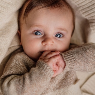 Bebé a usar camisola de malha bege e a morder as mãos