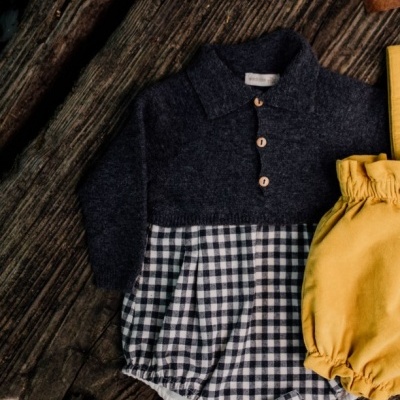 Roupa de bebé cinzento escuro e xadrez preto e branco com roupa amarela em fundo de madeira